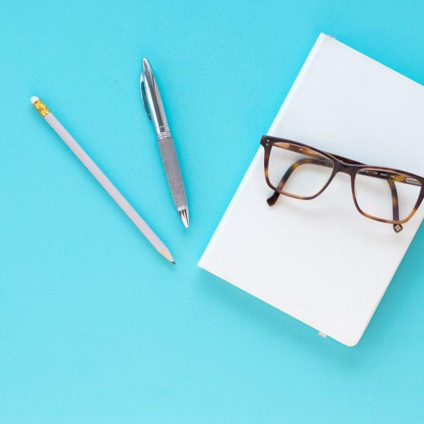 Notizbuch, Brille, Stifte auf türkisem Hintergrund