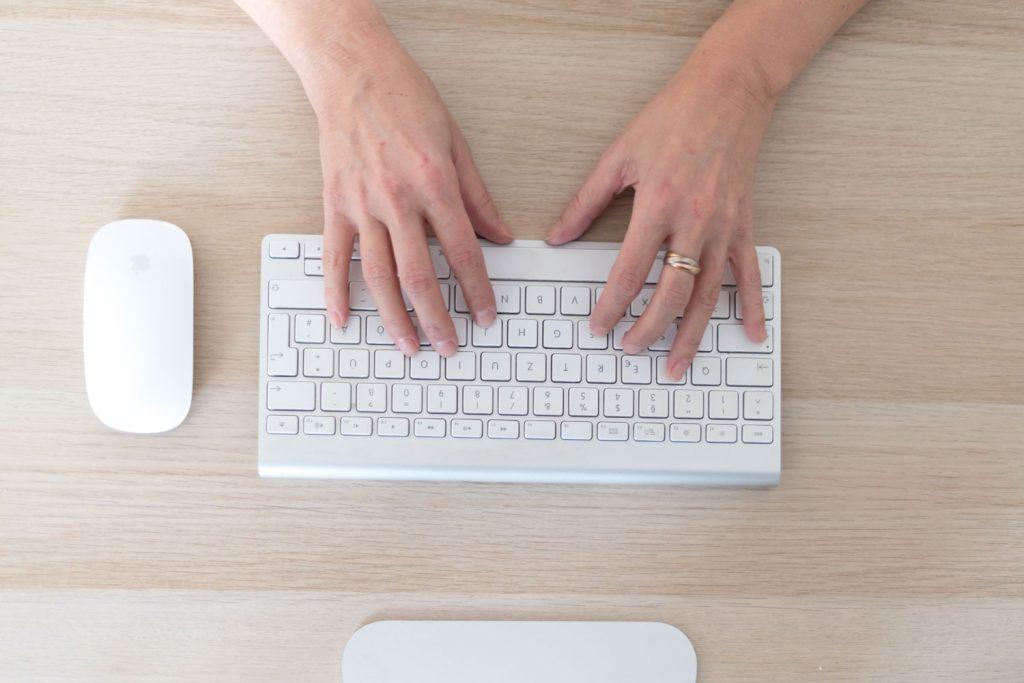 Sicht von oben auf eine Tastatur, Maus und zwei Hände - es werden SEO Tipps geschrieben