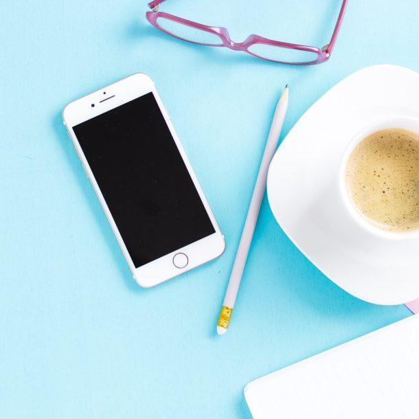 Man sieht eine Tasse Kaffee, Handy, Stift und Brille - es wird ein Beitrag über Quick Tipps im Online Marketing verfasst