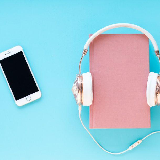 Flatlay Draufsicht: Türkiser Untergrund und darauf liegt ein Buch, Handy und Kopfhörer - Es geht um Fachbegriffe im Online Marketing