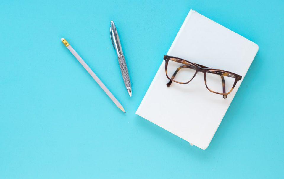 Flatlay zum Thema kostenloser Content - türkiser Untergrund und darauf liegt Stift, Block und eine Brille