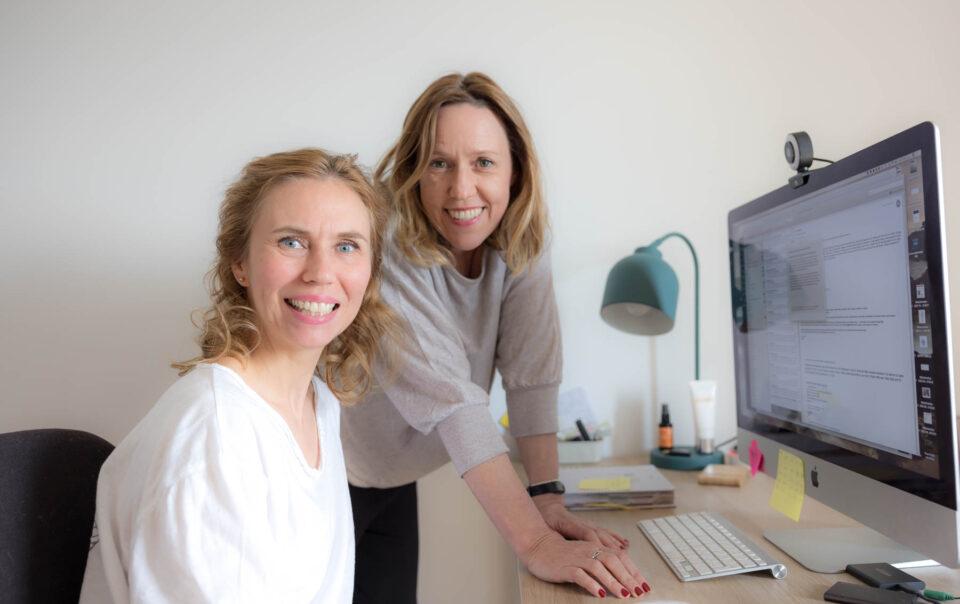 Nicola und Christina sitzen am Schreibtisch und arbeiten am Blogartikel: Noch keine E-Mail-Liste? Das kannst du jetzt tun